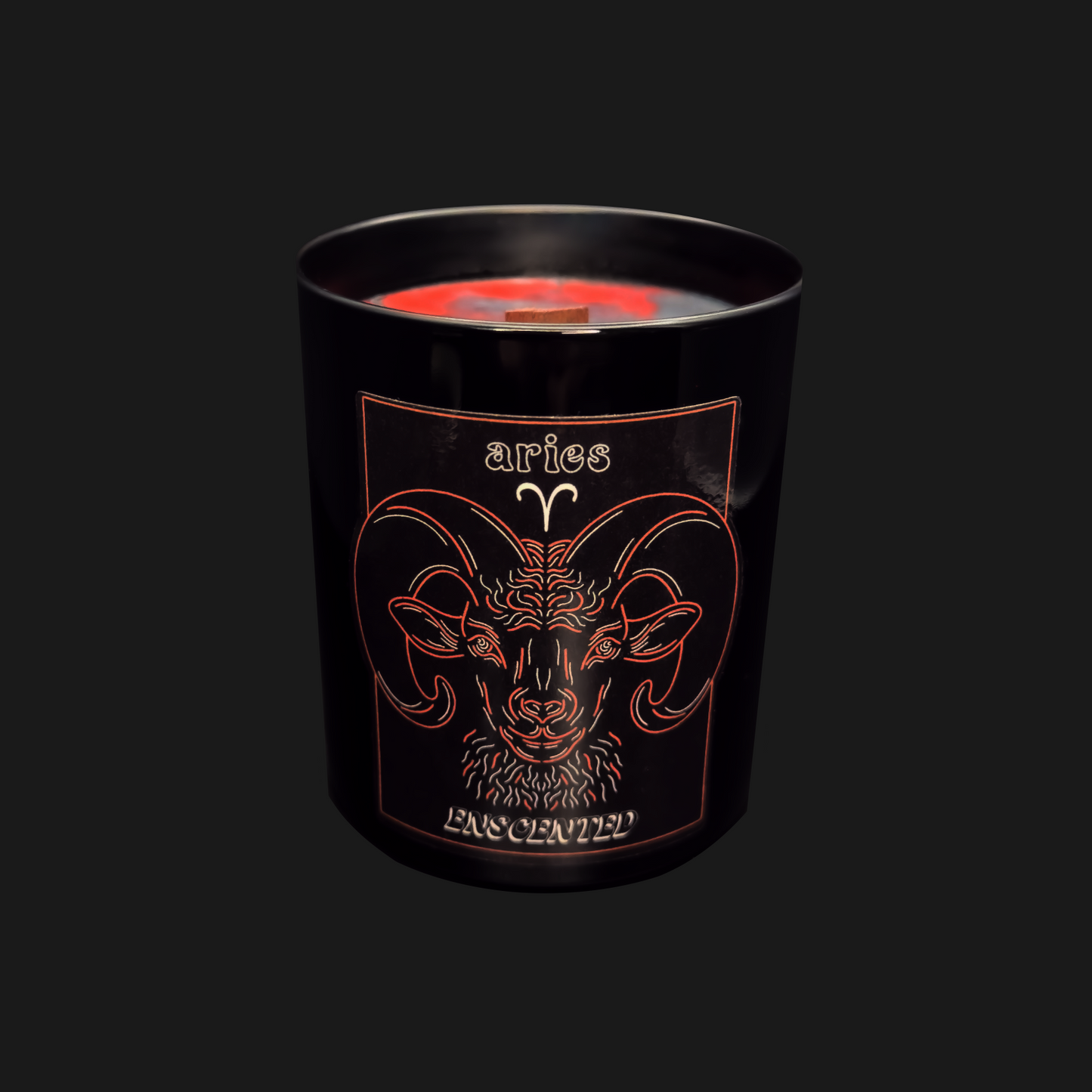 A black candle with a red tinted wax top, featuring an Aries astrological sign illustration in orange.