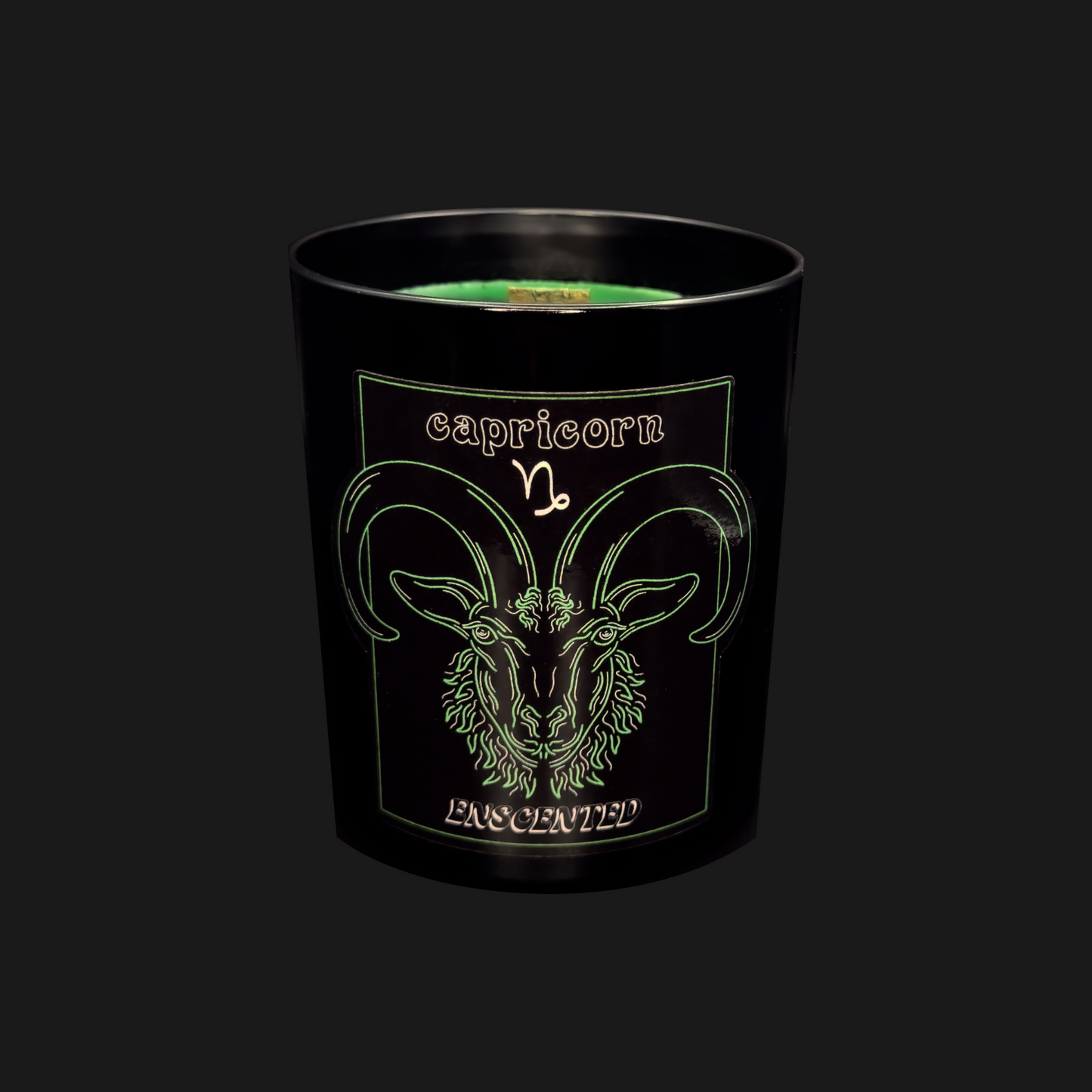 A black soy wax candle with a green tint, featuring the Capricorn zodiac sign illustration on the label.