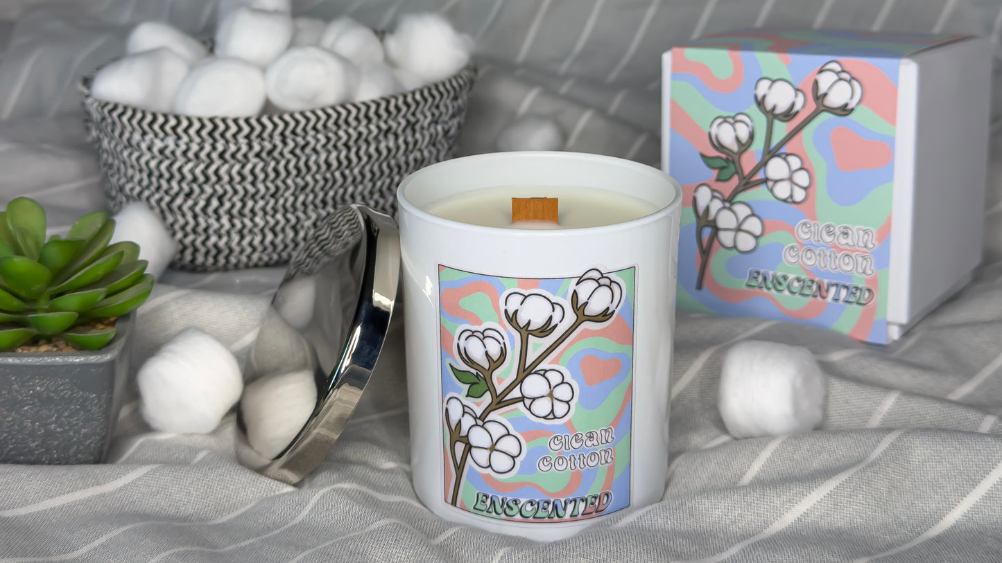 Candle with cotton design and packaging on a gray surface with cotton balls and a plant.
