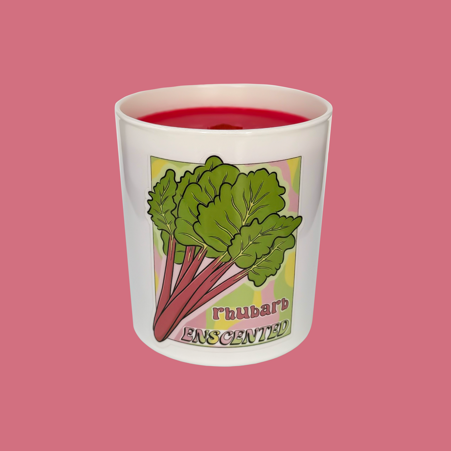 A white candle with a red tint on top, featuring an illustration of rhubarb leaves and the word 'RHUBARB' on the side, set against a pink background.