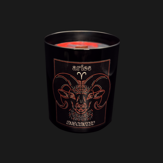 A black candle with a red tinted wax top, featuring an Aries astrological sign illustration in orange.