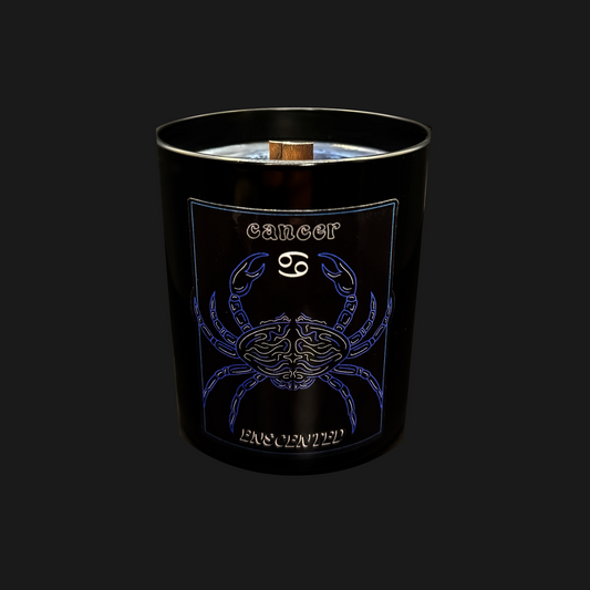 A black candle with a blue and white design featuring the Cancer zodiac sign as a crab, along with the name 'Cancer' written on it. The candle has a wooden wick and emits a slight frosted appearance.