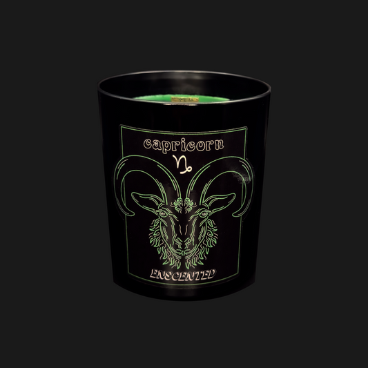 A black soy wax candle with a green tint, featuring the Capricorn zodiac sign illustration on the label.