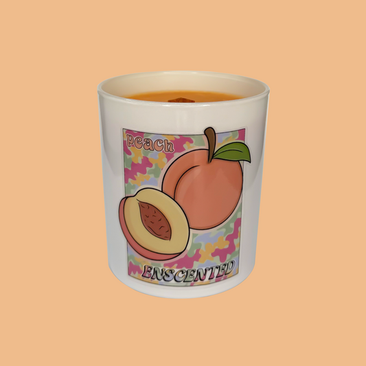 A white candle with a peach illustration and the word 'PEACHESCENTED' written on it, set against an orange background.
