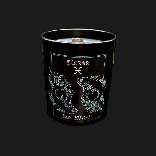 A black soy wax candle with a blue tint, engraved with the Pisces zodiac sign and a fish motif. The candle is unsliced, showing layered sections.