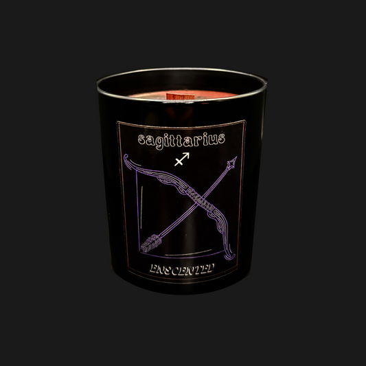 A black soy wax candle with a red candle wick, featuring a purple label with the Sagittarius zodiac sign.